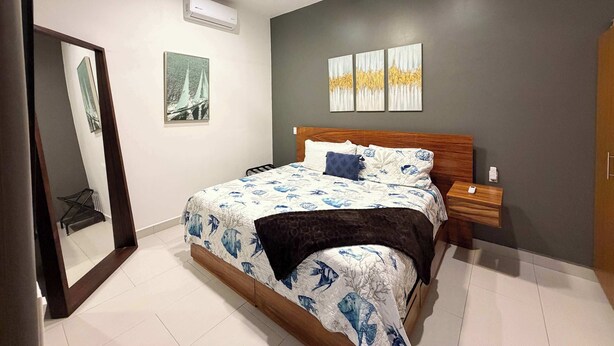 Un dormitorio con cama, ventilador de techo, aire acondicionado, espejo y obras de arte en la pared.