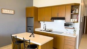 Cocina moderna con armarios de madera, un refrigerador de acero inoxidable, un microondas y un lavamanos. Hay dos taburetes de bar y una pequeña isla con un lavamanos.