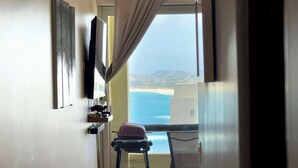 Habitación con vista al mar, una silla, una mesa y un televisor montado en la pared.