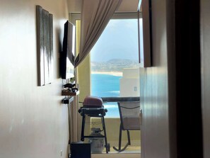 A room with a view of the sea, a chair, a table, and a television mounted on the wall. - Beachfront Arch View Balcony, Pool & Resort Access (Cabo San Lucas)