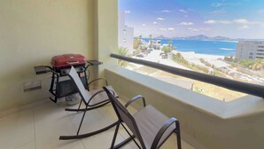 Un balcón con una parrilla, dos sillas y vista a la playa y al océano.