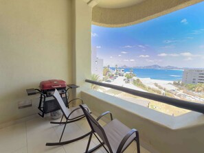 A balcony with a grill, two chairs, and a view of the beach and ocean. - Beachfront Arch View Balcony, Pool & Resort Access (Cabo San Lucas)