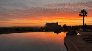 Piscina con vista al atardecer, sillas de descanso y una palmera.