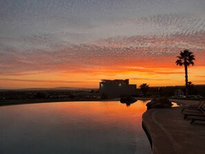 A swimming pool with a sunset view, lounge chairs, and a palm tree. - Beachfront Arch View Balcony, Pool & Resort Access (Cabo San Lucas)