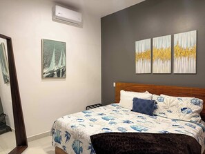 A bedroom with a bed, a wall-mounted air conditioner, and three paintings. - Beachfront Arch View Balcony, Pool & Resort Access (Cabo San Lucas)