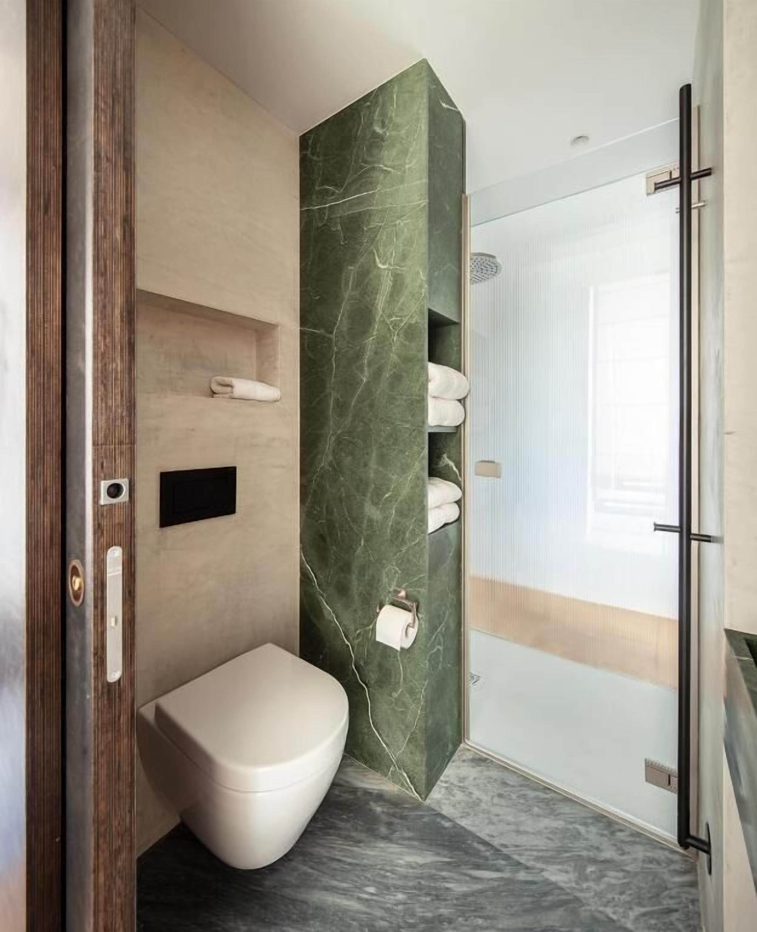 Un baño moderno con pared de mármol, inodoro, zona de ducha y puerta de cristal.