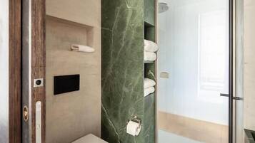 Un baño moderno con pared de mármol, inodoro, zona de ducha y puerta de cristal.