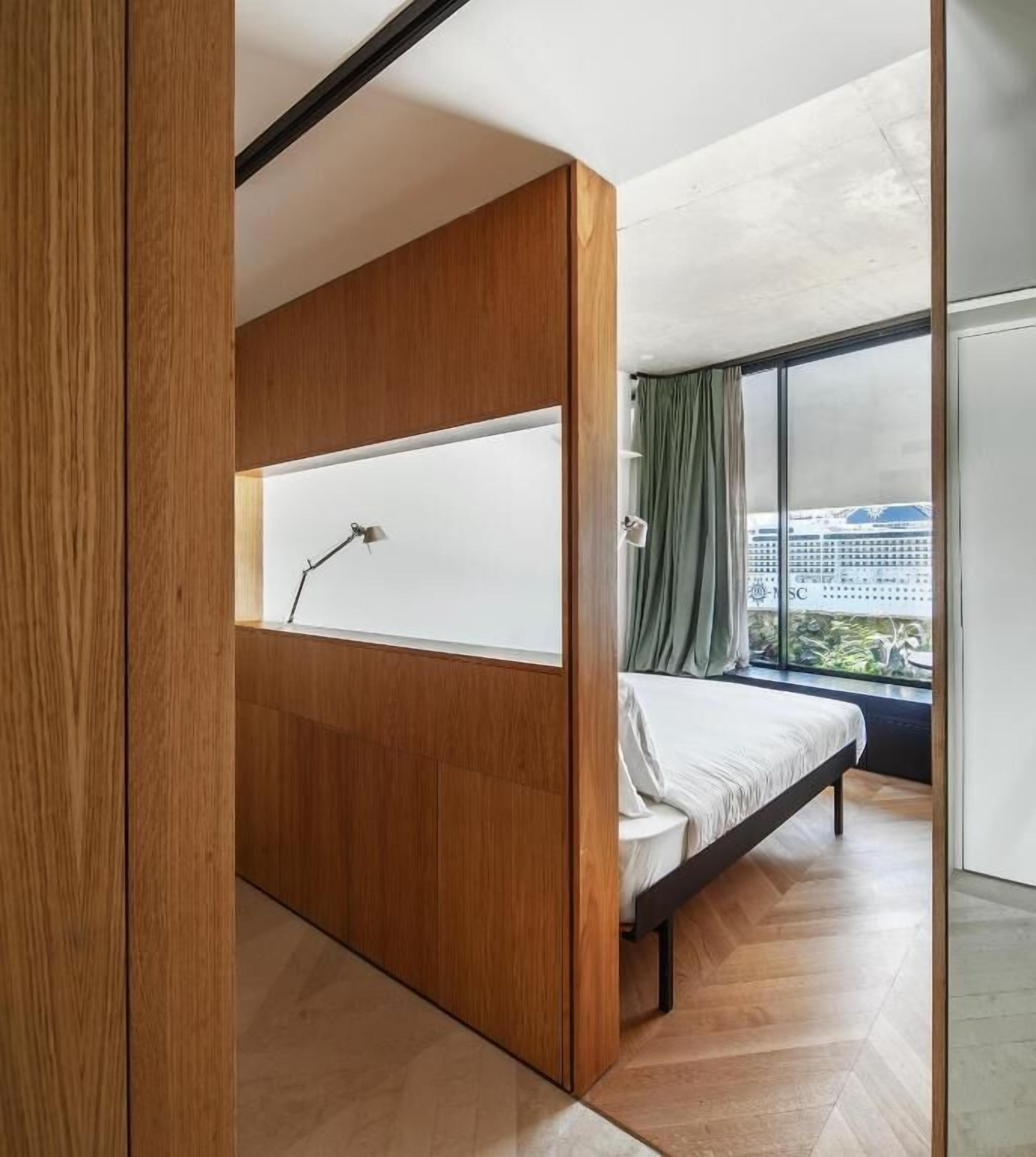 Un dormitorio con cama, ventana y vista a un edificio.