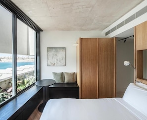 A hotel room with a large bed, a seating area with a view, a wooden wardrobe, and a painting on the wall.