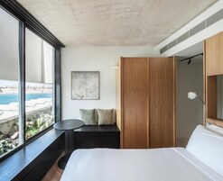A hotel room with a large bed, a seating area with a view, a wooden wardrobe, and a painting on the wall.