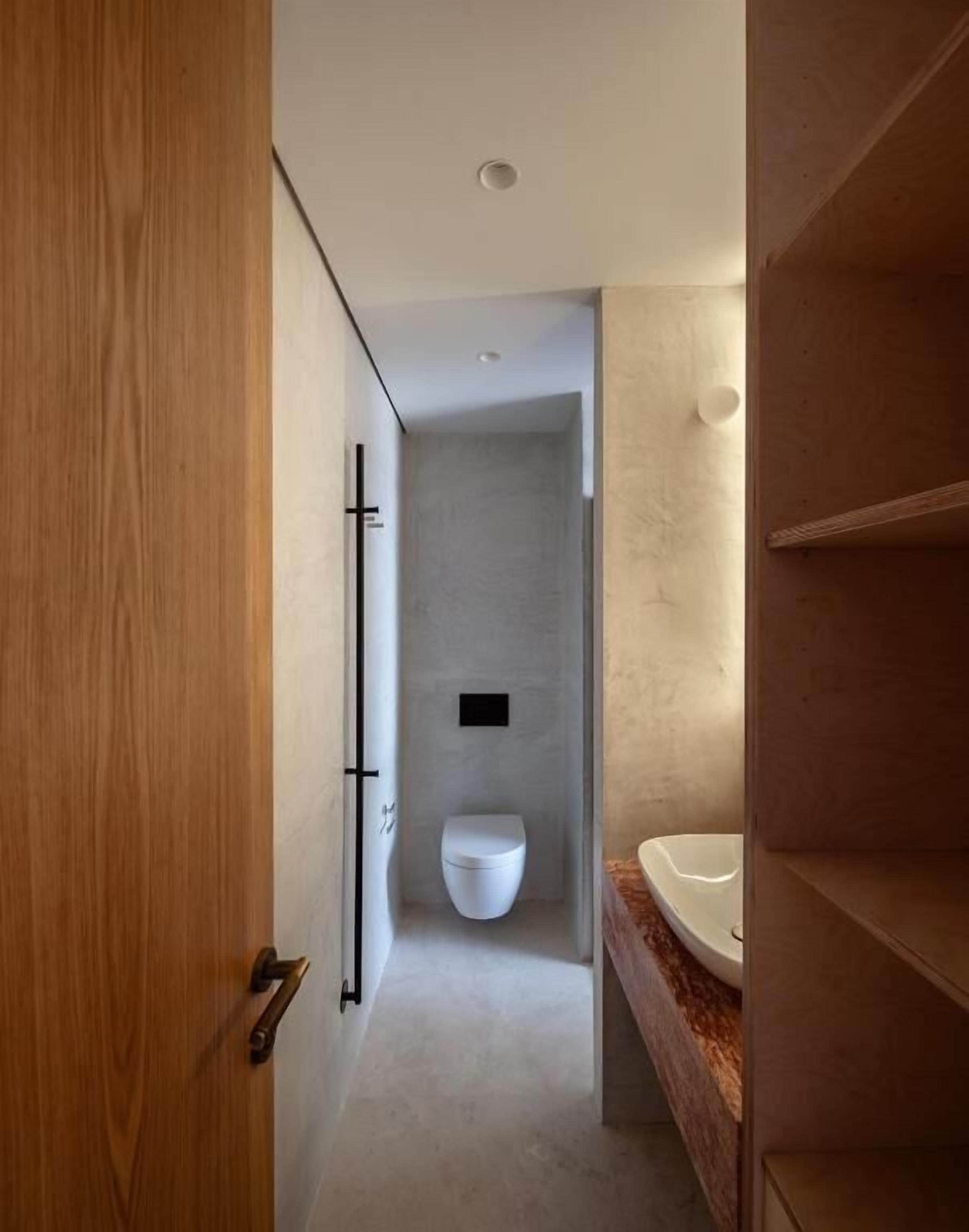 Un baño moderno con una puerta de madera, un inodoro blanco y un lavamanos con encimera de mármol.