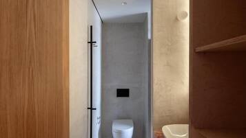 Un baño moderno con una puerta de madera, un inodoro blanco y un lavamanos con encimera de mármol.
