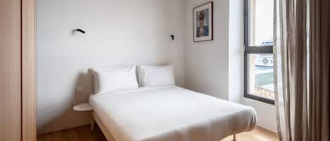 Un dormitorio con cama, ventana con cortinas y una pequeña mesa redonda.