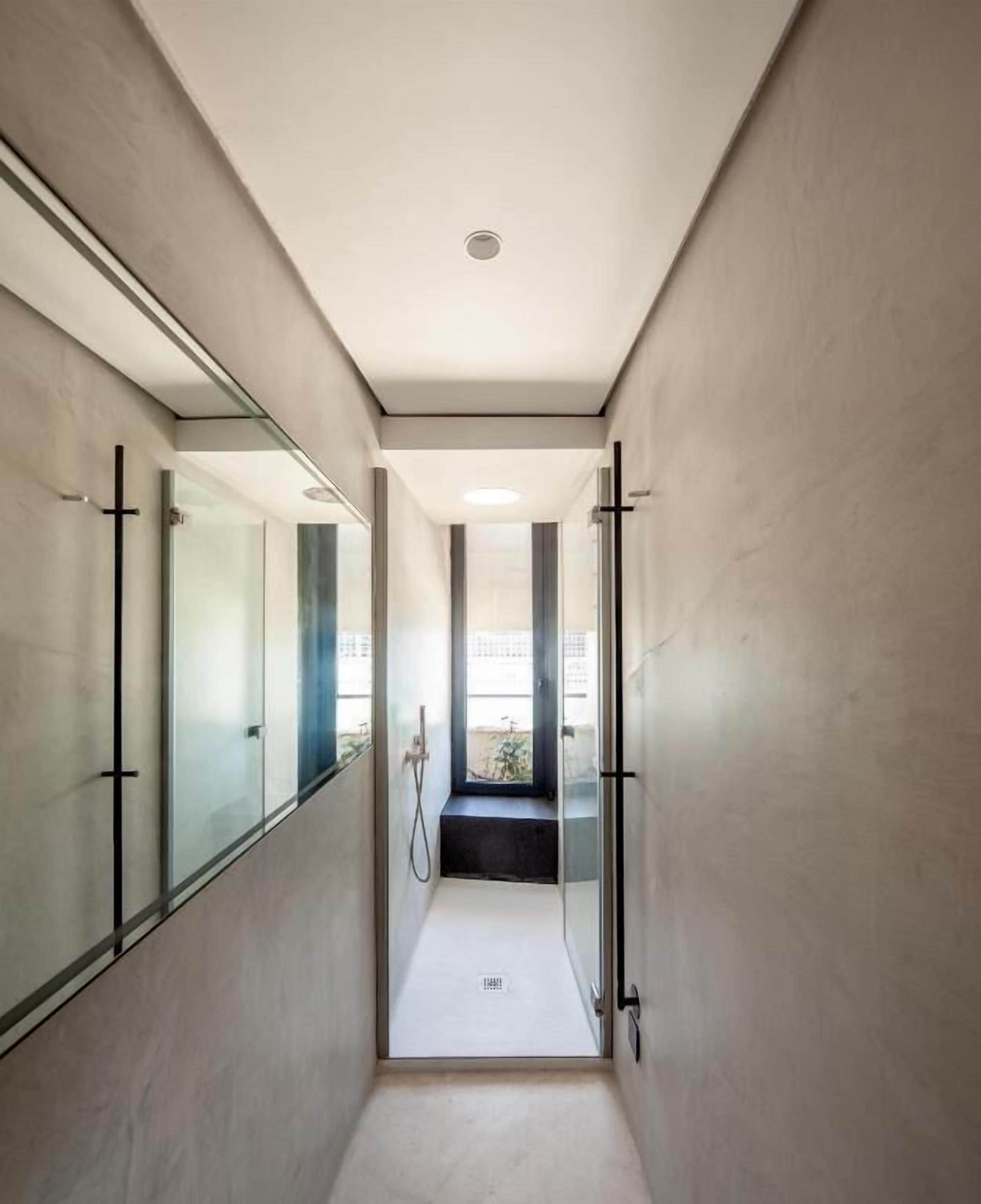 A narrow, modern hallway with glass doors leading to a bathroom.