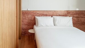 A bedroom with a wooden floor, a bed with white bedding, and a headboard with a textured design.