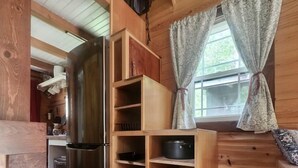 En inredning med träpanel, en inbyggd hyllsektion i trä, ett kylskåp i rostfritt stål och ett fönster med gardiner.