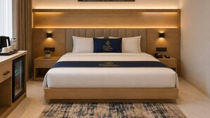 Habitación de hotel con una cama grande, dos mesitas de noche, un escritorio con cafetera y un cuadro enmarcado de un edificio en la pared.