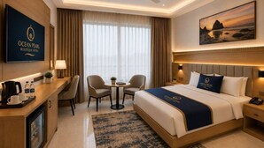 Habitación de hotel con cama, mesita de noche, lámpara, sillas, una pequeña mesa con una planta y un cuadro en la pared.