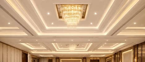 Un salón de banquetes con mesas redondas, sillas y una araña de cristal.