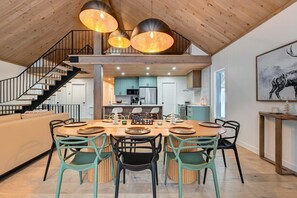 A modern kitchen with a central island, a dining area with a round table and chairs, and a staircase leading to an upper level. - Nayati Chalet | Luxury Chalet with Spa Near Mont-Tremblant (Amherst)