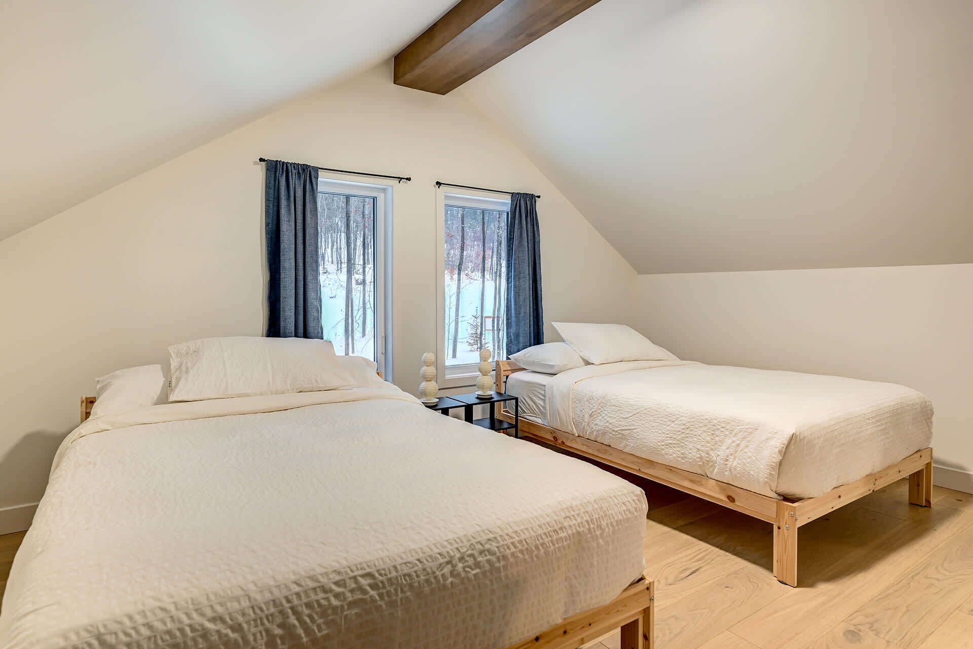 A room with two beds, wooden flooring, and a sloped ceiling.