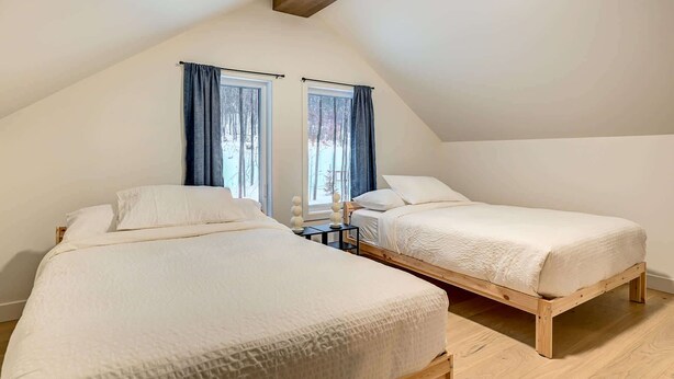Ein Zimmer mit zwei Betten, Holzboden und schrägverdeckter Decke.