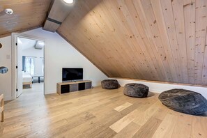 A loft-style room with a sloped ceiling, wooden flooring, a television, and two bean bags. - Nayati Chalet | Luxury Chalet with Spa Near Mont-Tremblant (Amherst)