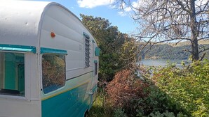 A vintage camper with a window and a door, surrounded by dense foliage and a clear sky. - Vintage Shasta Camper with Relaxing Fire Pit Escape on Geyserville, California (Geyserville)