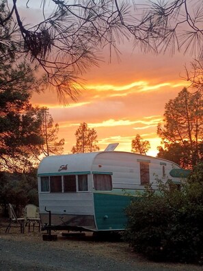 Una caravana vintage estacionada en un entorno natural, rodeada de árboles.