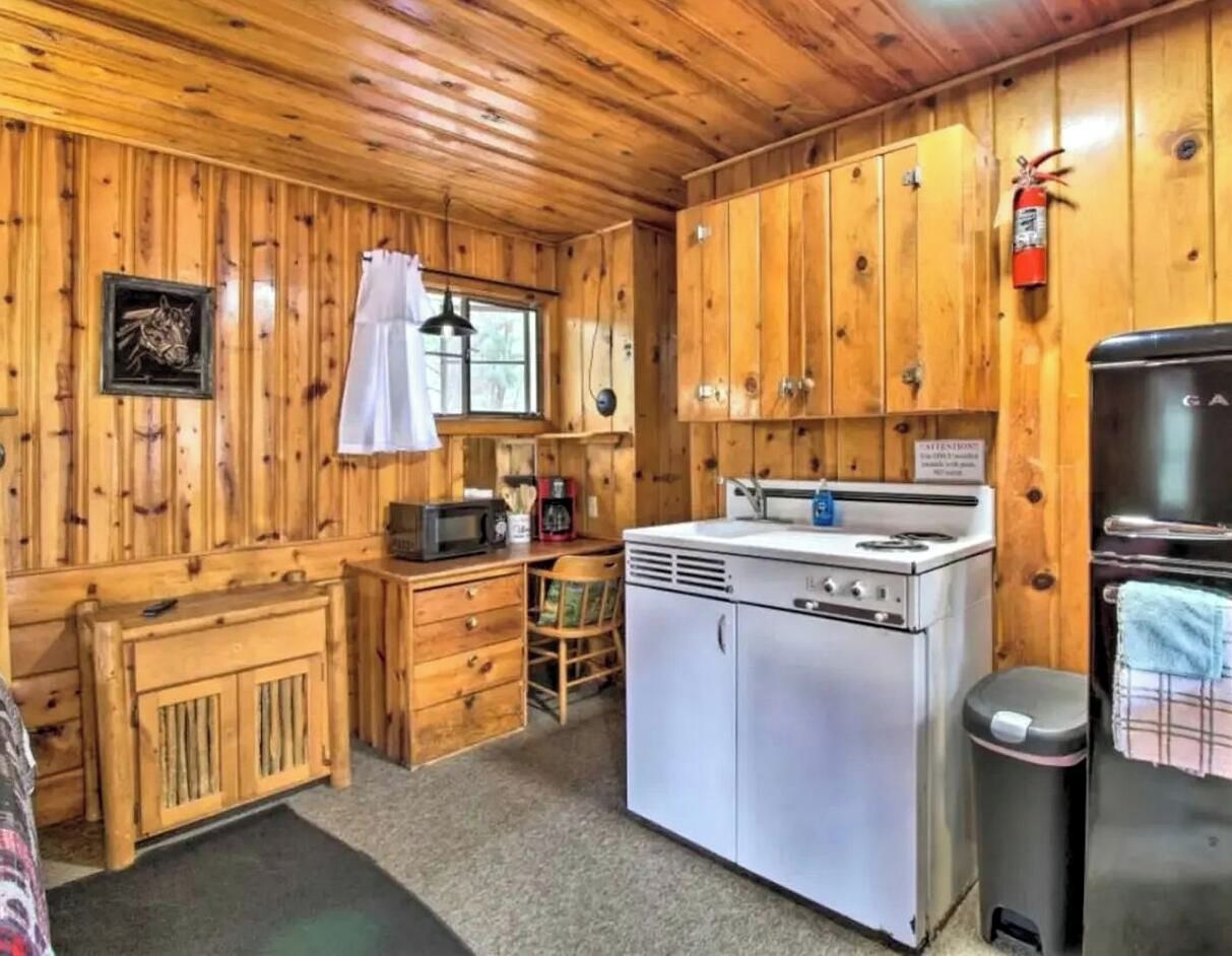 A cabin-style kitchen with wooden walls, a stove, a sink, and a refrigerator.