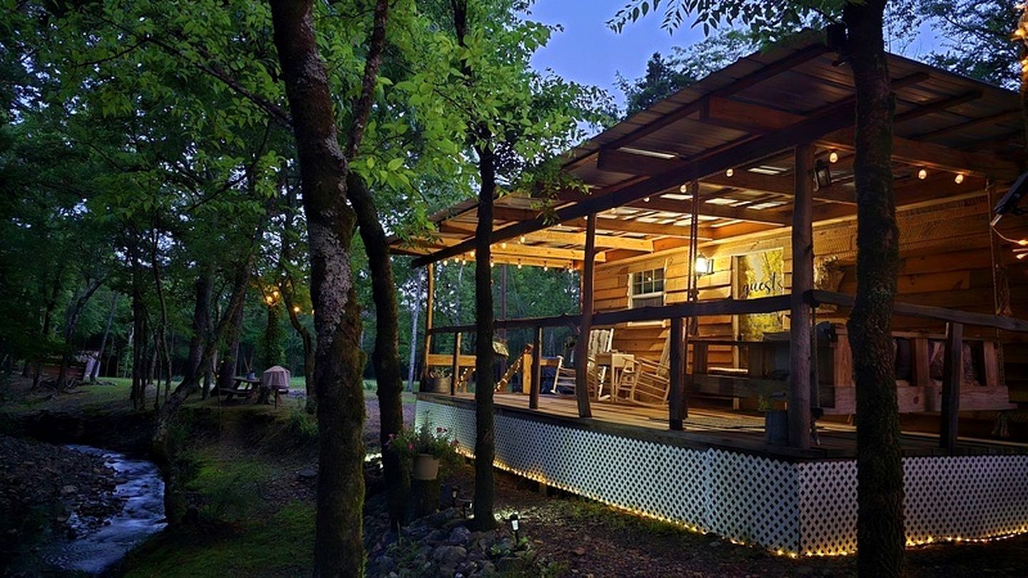 Eine Holzhütte mit einer Terrasse, umgeben von Bäumen und einem Bach.