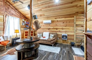 Interior acolhedor de uma cabana com uma mesa redonda, sofá e luminária pendente.