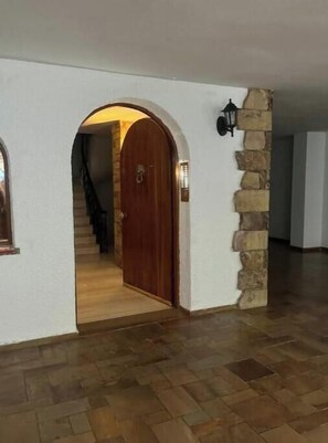 Ein Korridor mit einer Holztür, einer Steinsäule und einer Treppe, die in einen anderen Raum führt.