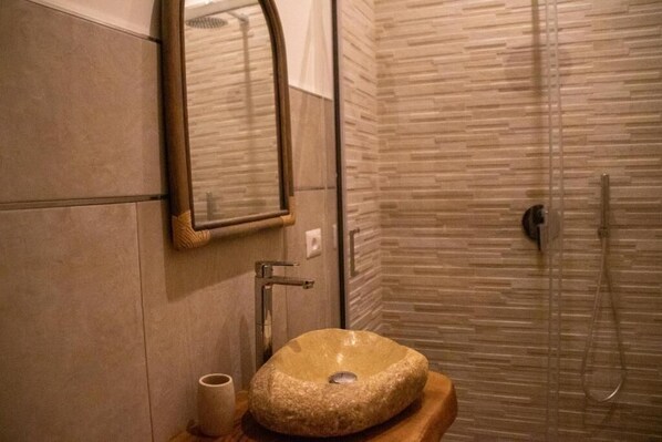 A bathroom with a stone sink, a mirror, and a shower area.