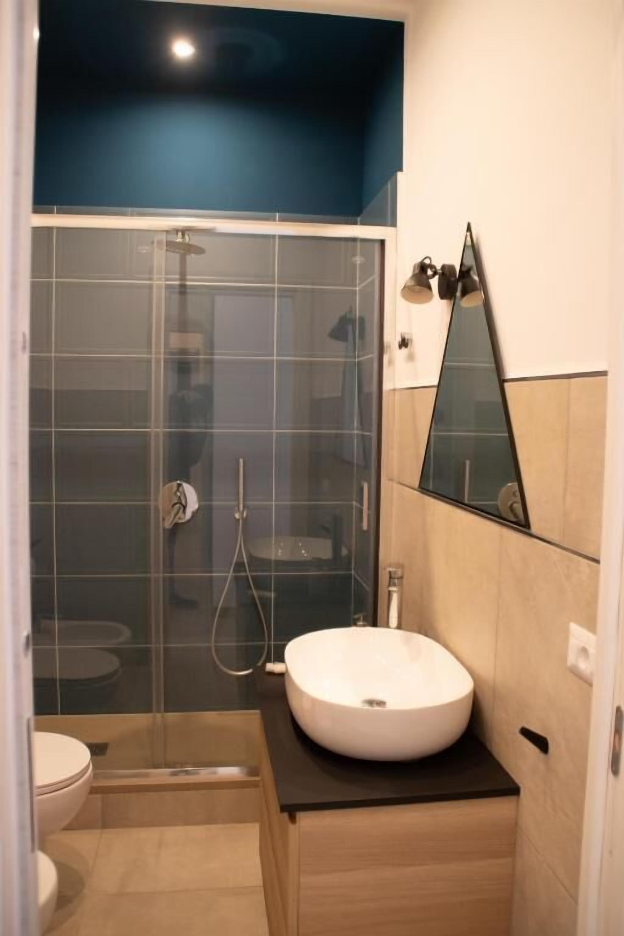 A bathroom with a glass shower enclosure, a white sink, and a mirror on the wall.