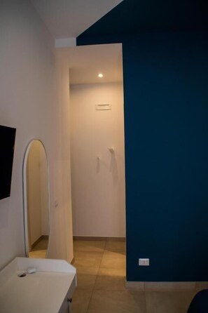 Une chambre d’hôtel avec une table de chevet blanche, un miroir, une porte donnant sur une autre pièce et un mur d’accent bleu.