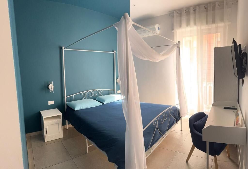 A bedroom with a four-poster bed, a bedside table, a chair, and a desk with a computer.
