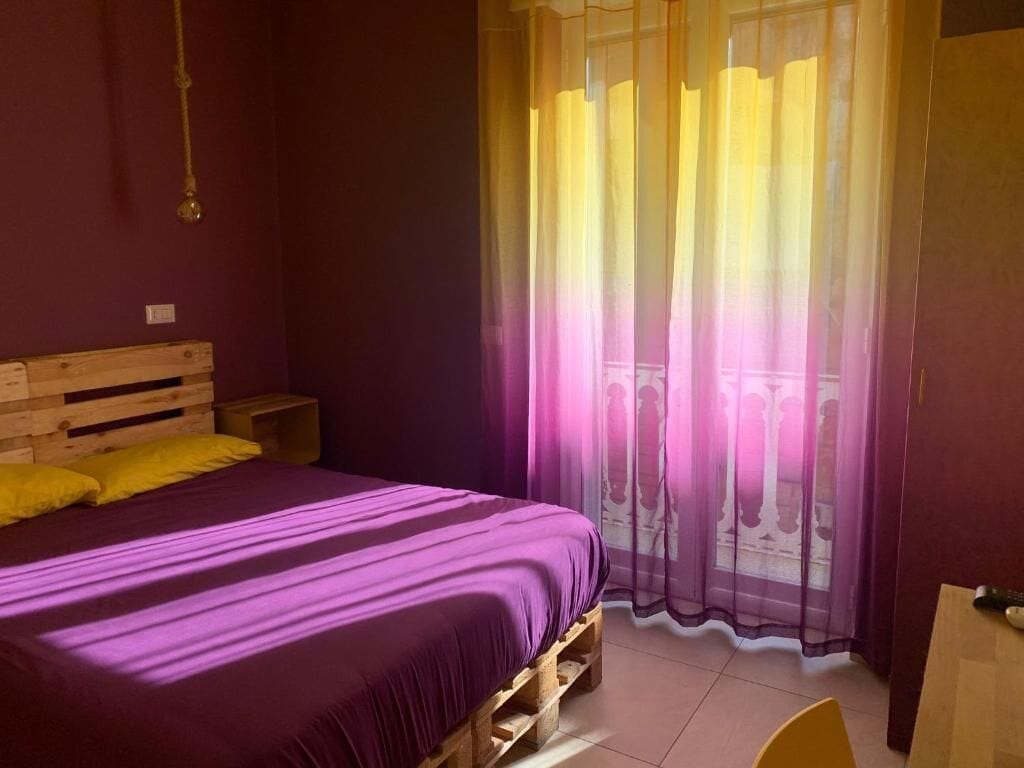 A room with a bed, wooden headboard, and a window with sheer curtains.