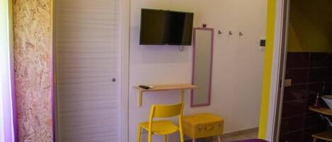 A room with a bed, a desk, a chair, a television, and a mirror.