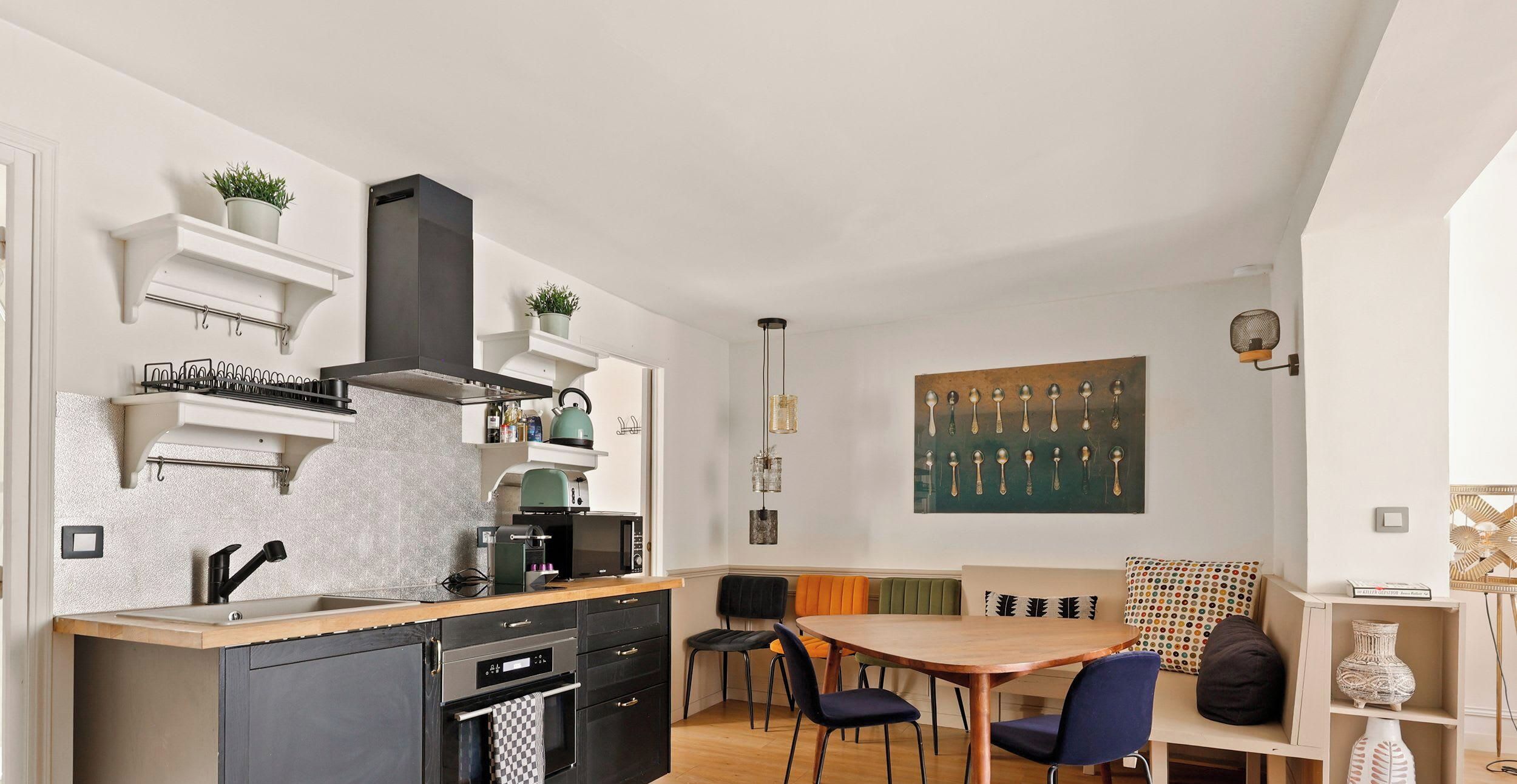 Eine kleine Küche mit modernen Geräten, ein Essbereich mit Holztisch und Stühlen sowie ein Kunstwerk an der Wand.