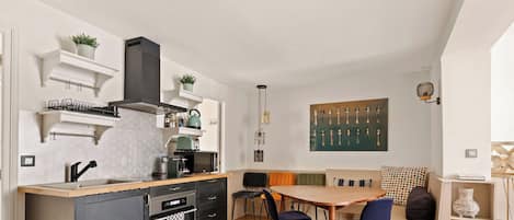 Eine kleine Küche mit modernen Geräten, ein Essbereich mit Holztisch und Stühlen sowie ein Kunstwerk an der Wand.