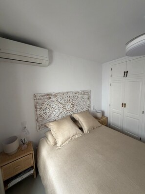 Ein Schlafzimmer mit einem Bett, einem Nachttisch, einer Klimaanlage, einem Kleiderschrank und einem dekorativen Kopfteil.