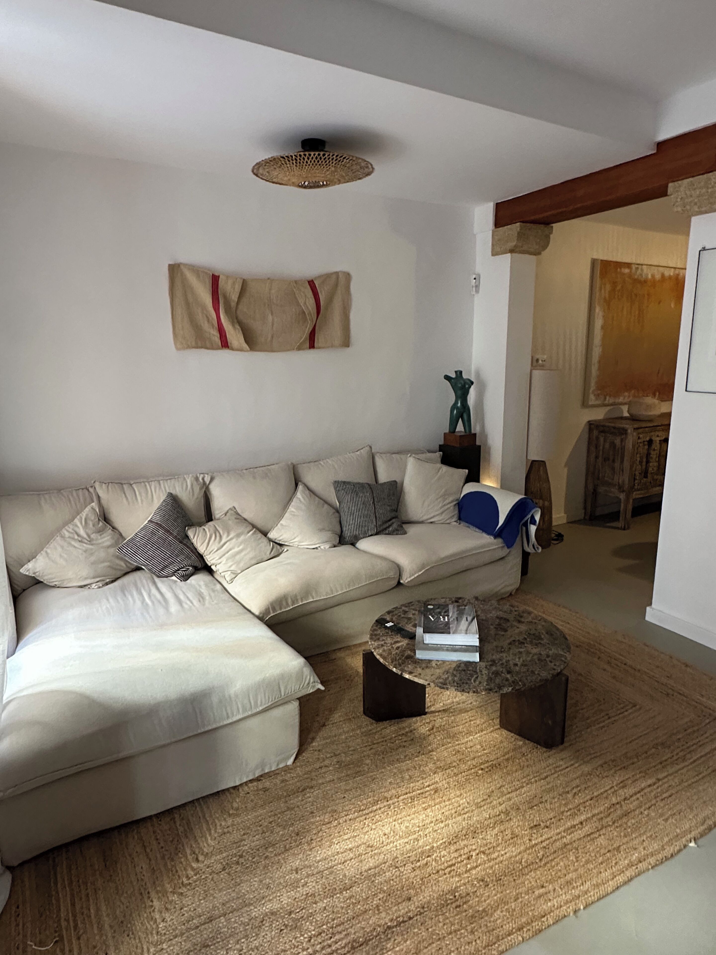 Een woonkamer met een beige hoekbank, een ronde salontafel en een geweven vloerkleed.