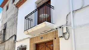 Edifici de dues plantes amb un balcó, una porta de fusta amb una reixa de metall i el número '19' visible a la paret.