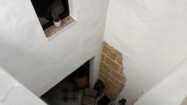 Unes escales estretes amb parets blanques i una paret de pedra d'un costat. Hi ha plantes en testos, una cistella de vimet i un paviment de rajoles.