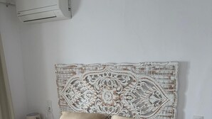 Un dormitori amb un llit, dues taules de nit, un aparell d'aire condicionat i una obra decorativa a la paret.