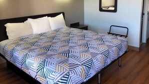 Habitación de hotel con cama, mesita de noche, espejo en la pared y una puerta.