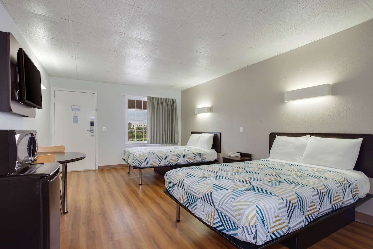A hotel room with two beds, a desk, a television, and a window with curtains.