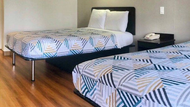Habitación de hotel con dos camas, una mesita de noche con teléfono y una lámpara de pared.