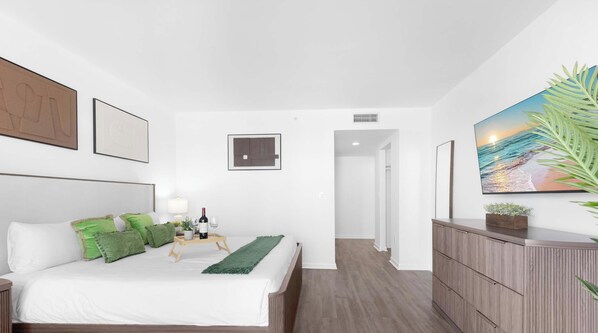 A modern bedroom with a bed, bedside table, lamp, and artwork. - Stylish Haven with Pool & Private Balcony! (Hallandale Beach)